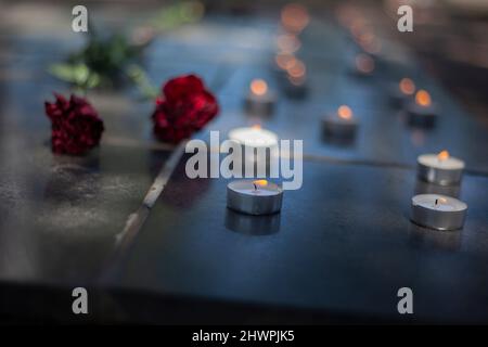 Kerzen auf Grabstein. Wachskerzen brennen auf dem Kriegsdenkmal. Zwei Blumen auf Grabstein. Begräbnisstätte der Soldaten. Memorial Complex im Detail. Stockfoto