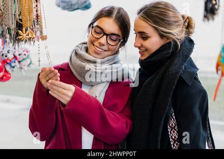 Lächelnde junge Freunde, die den Rosenkranz auf dem Markt betrachten Stockfoto