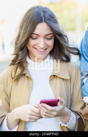 Lächelnde Frau, die Smartphone auf dem Universitätsgelände benutzt Stockfoto