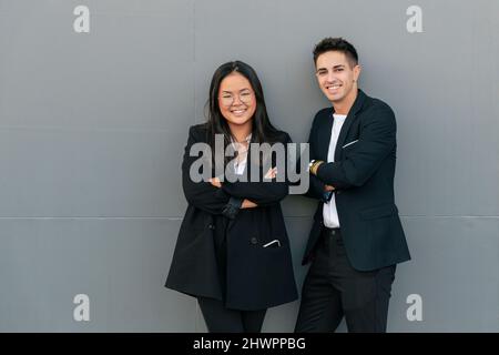 Junger Geschäftsmann mit Geschäftsfrau, die sich an einer grauen Wand lehnt Stockfoto