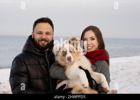 Lächelndes junges Paar mit australischem Schäferhund am Strand Stockfoto