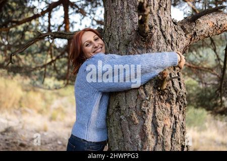 Lächelnde Frau umarmt Baumstamm im Park Stockfoto