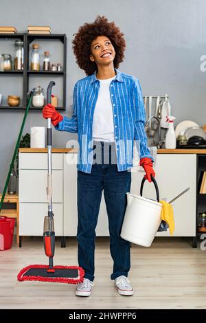 Nachdenkliche junge Afro-Frau mit Reinigungseimer und Wischmopp in der Küche Stockfoto