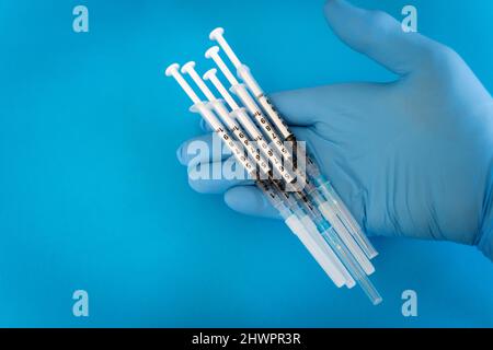 Arzt hält Spritzen vor blauem Hintergrund im Studio Stockfoto