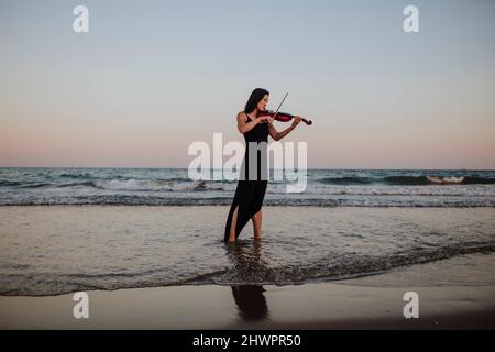 Frau spielt Geige vor klarem Himmel bei Sonnenuntergang Stockfoto