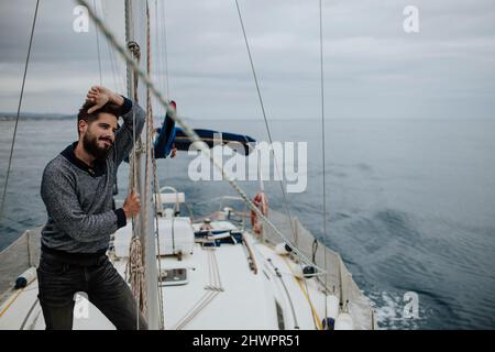 Nachdenklicher Mann, der sich im Mittelmeer auf den Mast eines Segelbootes stützt Stockfoto