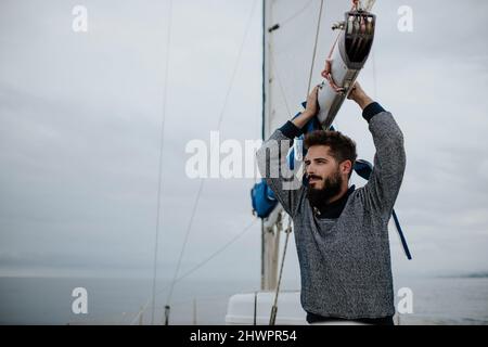 Nachdenklicher junger Mann, der sich im Mittelmeer auf den Mast eines Segelbootes stützt Stockfoto