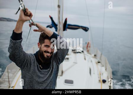 Lächelnder junger Mann, der ein Segelschiff im Mittelmeer hält Stockfoto