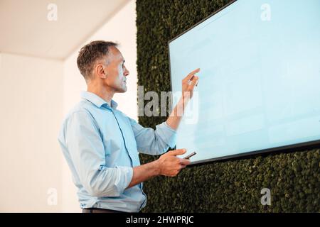 Reifer Geschäftsmann zeigt auf Touchscreen-Computermonitor im Coworking-Büro Stockfoto