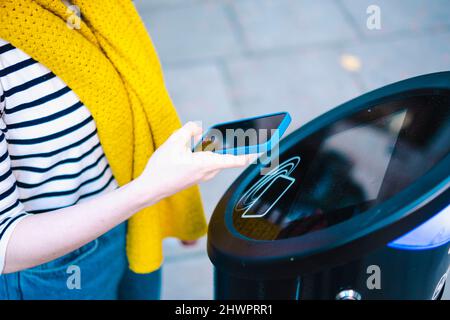 Frau, die an der Ladestation kontaktlos über das Smartphone bezahlt Stockfoto