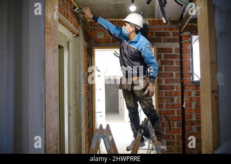Elektriker, der mit dem Werkzeug auf der Leiter auf der Baustelle arbeitet Stockfoto