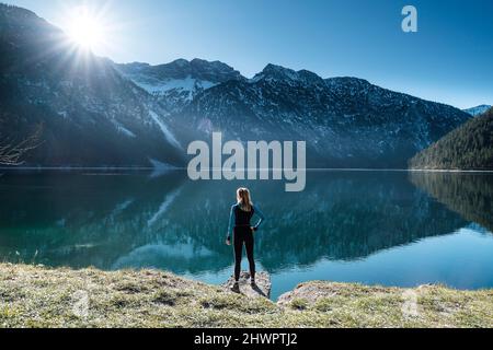 Frau mit Hand an der Hüfte über den Plansee bis zu den Ammergauer Alpen, Reutte, Tirol, Österreich Stockfoto