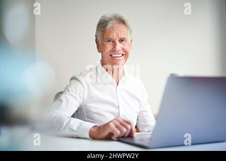 Lächelnder Geschäftsmann mit Laptop am Schreibtisch im Studio Stockfoto