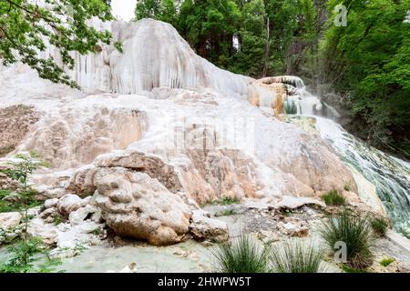 Weißer Felsen la Balena Bianca von natürlichen Thermalwasserfall und üppigem Grün in Bagni San Filippo. Toskana, Italien Stockfoto