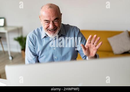 Fröhlicher Freiberufler, der bei einem Videoanruf über den Desktop-Computer im Heimbüro mit der Hand winkt Stockfoto