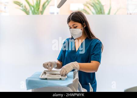 Krankenschwester trägt eine schützende Gesichtsmaske, die zahnärztliche Ausrüstung in der medizinischen Klinik arrangiert Stockfoto