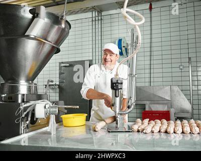 Glückliche Metzgerei, die Würste durch Maschinen in der Fabrik herstellt Stockfoto