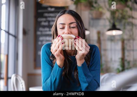 Glückliche Frau trinkt Cappuccino im Café Stockfoto