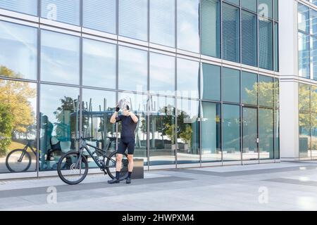 Junge Radfahrerin mit Fahrradhelm vor dem Bürogebäude Stockfoto