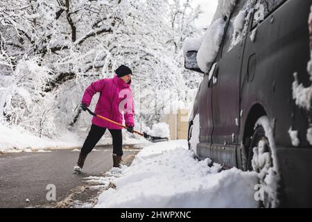 Mann schaufelt Schnee um Auto in der Wintersaison Stockfoto