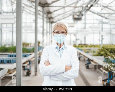 Wissenschaftler trägt eine schützende Gesichtsmaske in der Pflanzenzügnerei Stockfoto