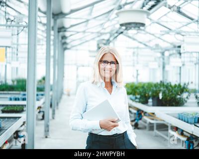 Glücklicher Wissenschaftler mit Tablet-PC in der Baumschule Stockfoto