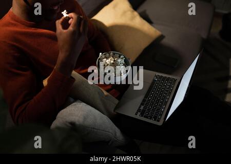 Mann, der sich einen Film auf dem Laptop ansieht und zu Hause Popcorn isst Stockfoto