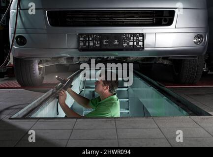 Automechaniker mit Taschenlampe, die in der Werkstatt unter dem Auto arbeitet Stockfoto