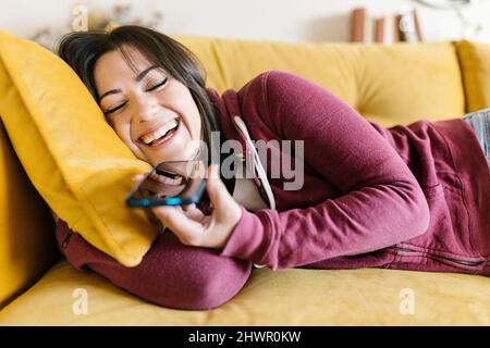 Fröhliche Frau, die zu Hause über Lautsprecher auf dem Smartphone spricht Stockfoto