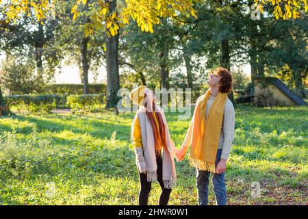 Lächelndes Paar, das die Hände hält und im Herbstpark nach oben schaut Stockfoto