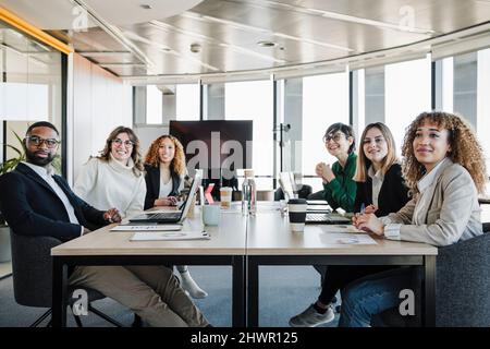 Lächelnder Geschäftsmann und Geschäftsfrauen, die an einem Konferenztisch sitzen Stockfoto