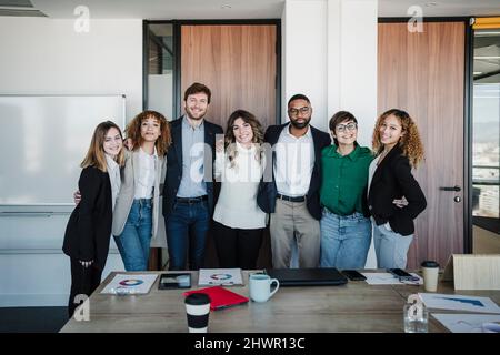 Lächelnde Geschäftsmänner und Geschäftsleute, die mit den Armen im Konferenzraum stehen Stockfoto