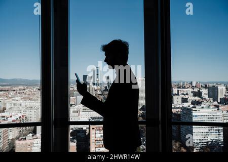 Silhouette eines Geschäftsmanns, der im Büro ein Smartphone an einer Glaswand verwendet Stockfoto