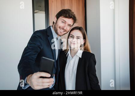 Geschäftsmann und Geschäftsfrau nehmen Selfie über Mobiltelefon im Büro Stockfoto