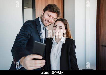 Lächelnder Geschäftsmann, der mit einem Kollegen im Büro ein Selfie über das Smartphone gemacht hat Stockfoto
