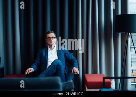 Selbstbewusster Geschäftsmann, der im Büro auf einem Stuhl sitzt Stockfoto