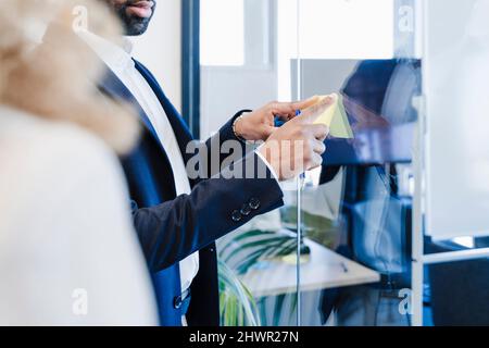 Geschäftsmann klebt im Büro eine Haftnotiz auf das Glas Stockfoto
