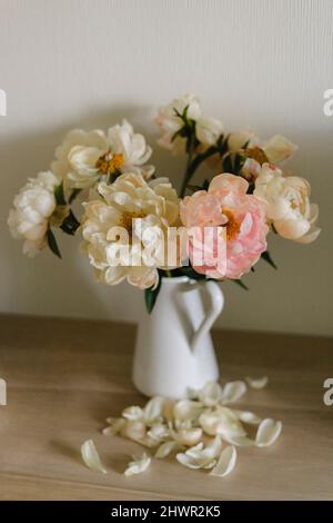 Verwelkt Pfingstrosen in Vase von Blütenblättern auf Tisch Stockfoto