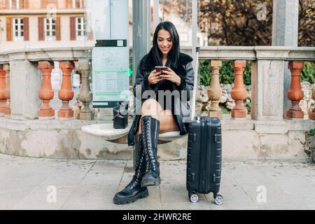 Lächelnde Frau mit Smartphone auf der Bank sitzen Stockfoto