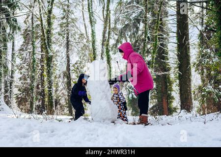 Vater mit Töchtern, die Schneemann im Winterwald bauen Stockfoto