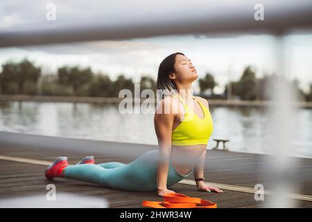Aktive Frau, die Cobra-Stretch mit geschlossenen Augen auf dem Steg macht Stockfoto