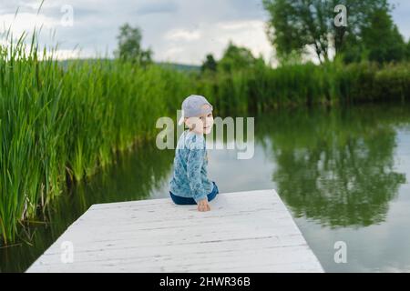 Junge, der auf dem Steg am See über die Schulter schaut Stockfoto