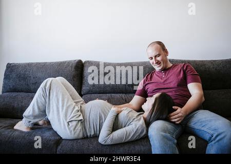 Schwangere, die zu Hause auf dem Schoß des Mannes auf dem Sofa liegt Stockfoto