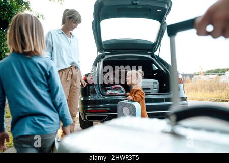 Mutter schaut im Urlaub Tochter mit Koffer mit dem Kofferraum an Stockfoto