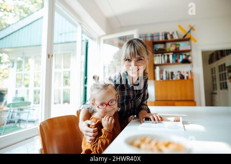 Lächelnde Mutter mit Arm um Tochter zu Hause Stockfoto