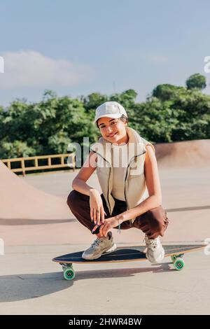 Lächelnde Frau, die im Park auf dem Skateboard hockt Stockfoto