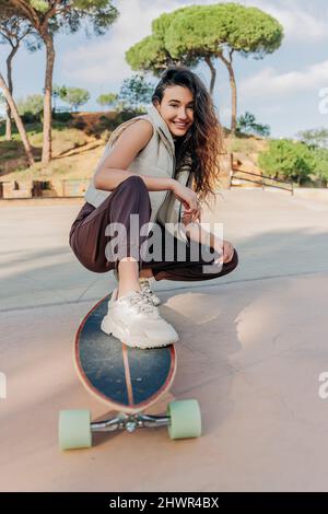 Lächelnde Frau, die im Park mit Skateboard hockt Stockfoto