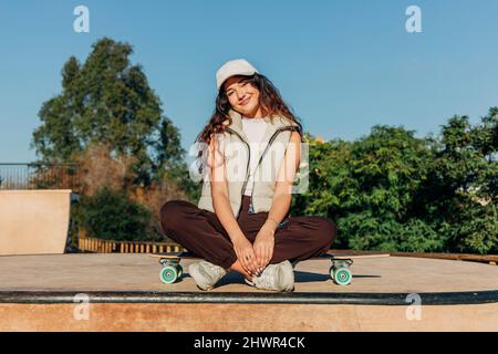 Lächelnde Frau, die an einem sonnigen Tag über dem Skateboard sitzt Stockfoto