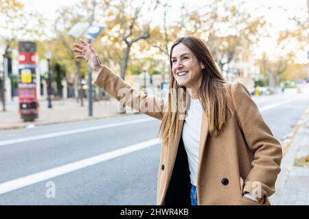 Eine glückliche Frau, die ein Taxi auf der Stadtstraße anhagelt Stockfoto