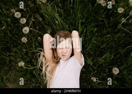 Nettes Mädchen, das inmitten von Dandelionen auf dem Feld liegt Stockfoto